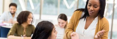 Hochschulprofessorin spricht mit Studierenden in einem Seminarraum.