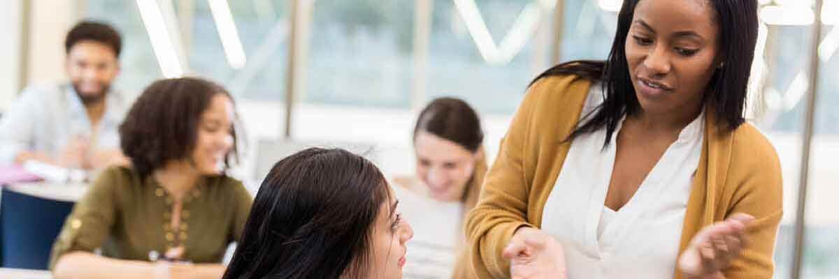 Hochschulprofessorin spricht mit Studierenden in einem Seminarraum.