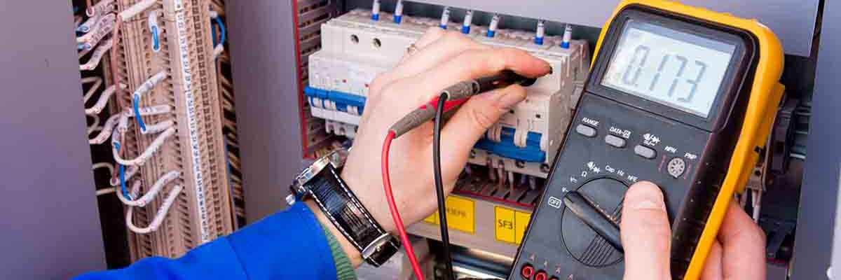 Elektriker arbeitet an einem elektrischen Panel mit Sicherheitshelm und Werkzeug.
