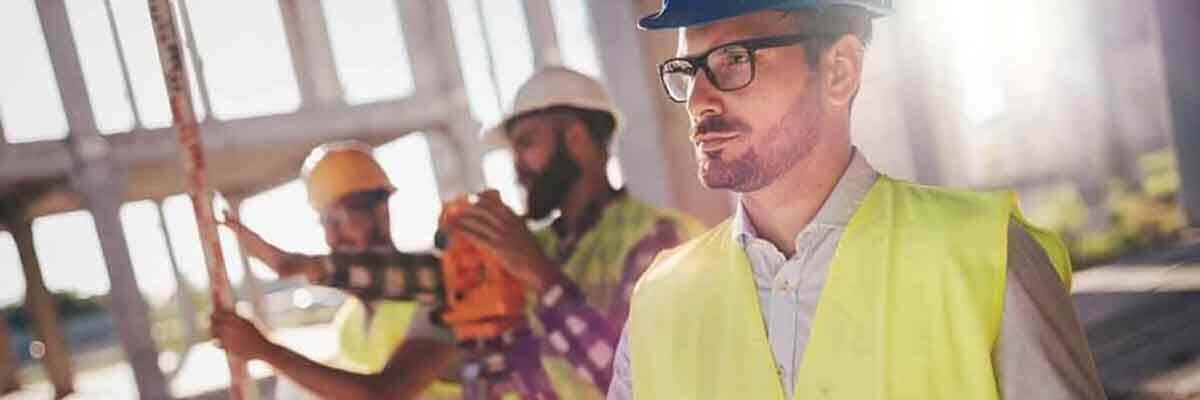 Bauingenieur im Helm überprüft Baupläne auf einer aktiven Großbaustelle.