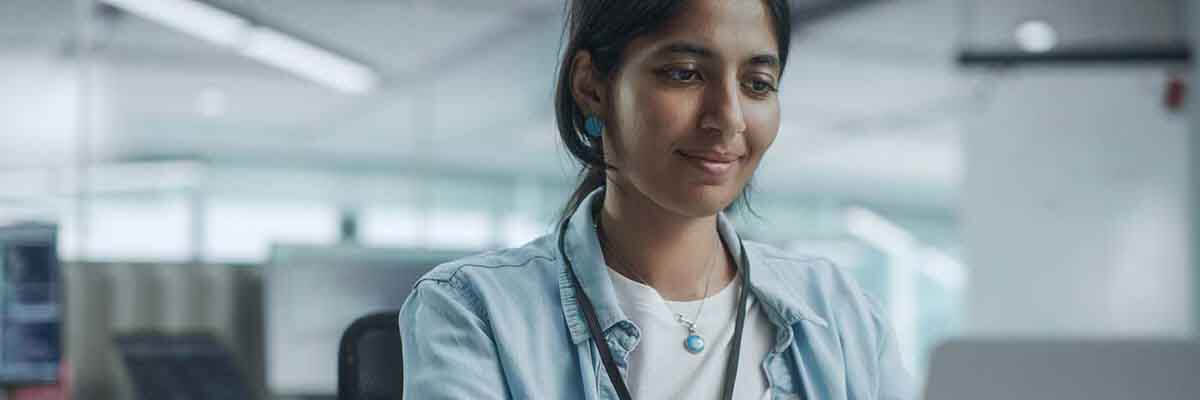 Wirtschaftsinformatiker – Perspektiven, Branchen & Zukunftschancen Porträt einer lächelnden Programmiererin in einem Büro mit Kollegen im Hintergrund.