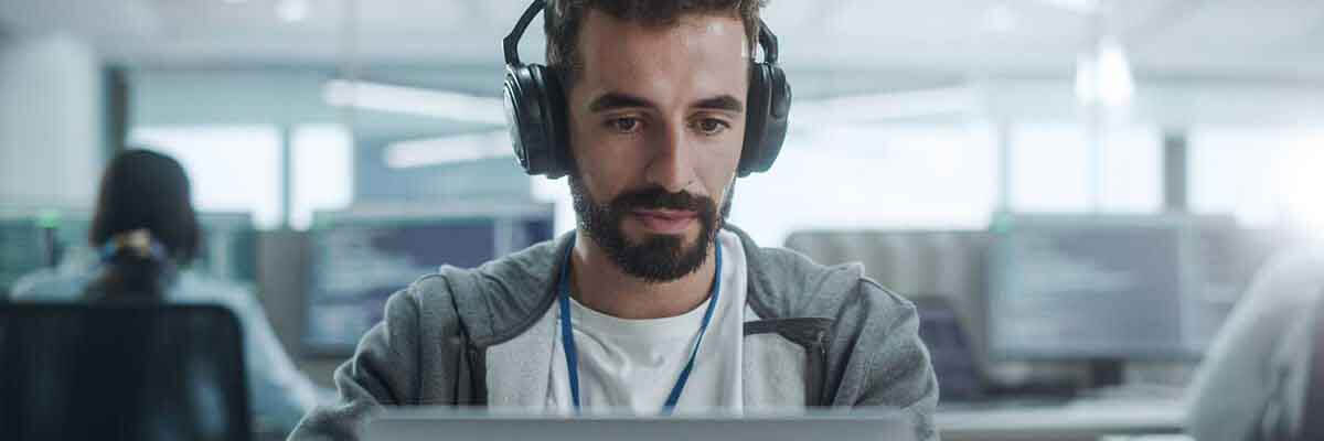 Lächelnder IT-Programmierer mit Kopfhörern arbeitet an einem Computer in einem modernen Büro.