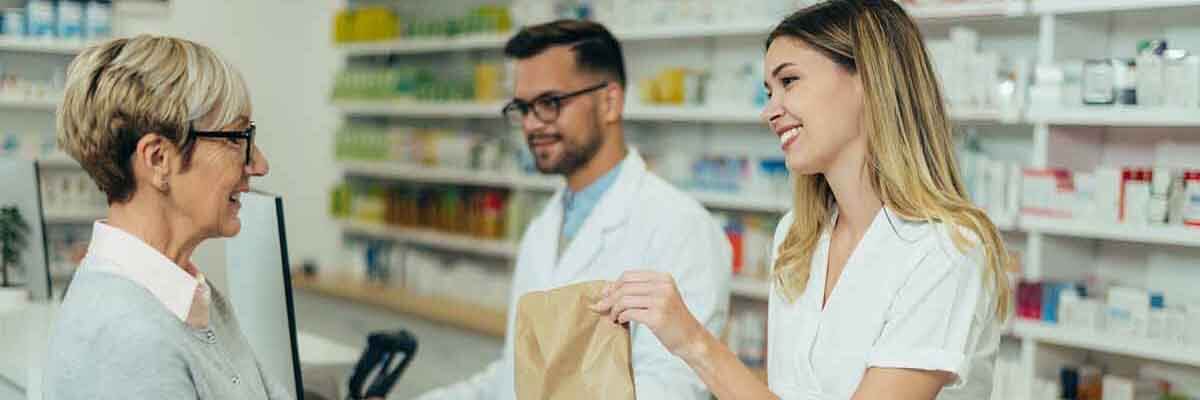 Zwei Apotheker geben einem älteren weiblichen Kunden verschreibungspflichtige Medikamente in einer Apotheke.