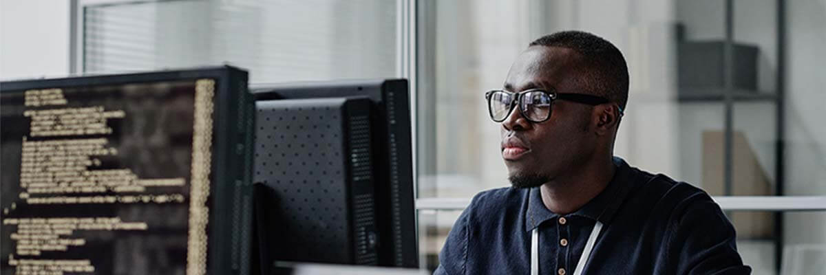 Softwareentwickler schaut auf Bildschirm. Im Vordergrund ist ein Monitor mit Code zu sehen.