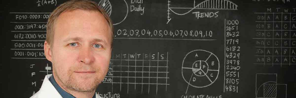 Universitätsprofessor steht vor einer Tafel in einem Hörsaal und hält einen Vortrag.