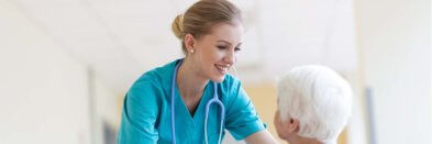 Pflegefachkraft spricht mit älterer Dame im Rollstuhl