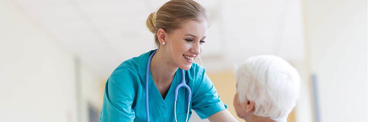 Pflegefachkraft spricht mit älterer Dame im Rollstuhl